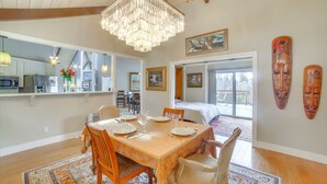 A dining area with a large wooden table, chairs, and a chandelier. There is a kitchen area with modern appliances and a dining table with plates and glasses set. - Redwood Retreat Near Beach & Trails (Aptos)