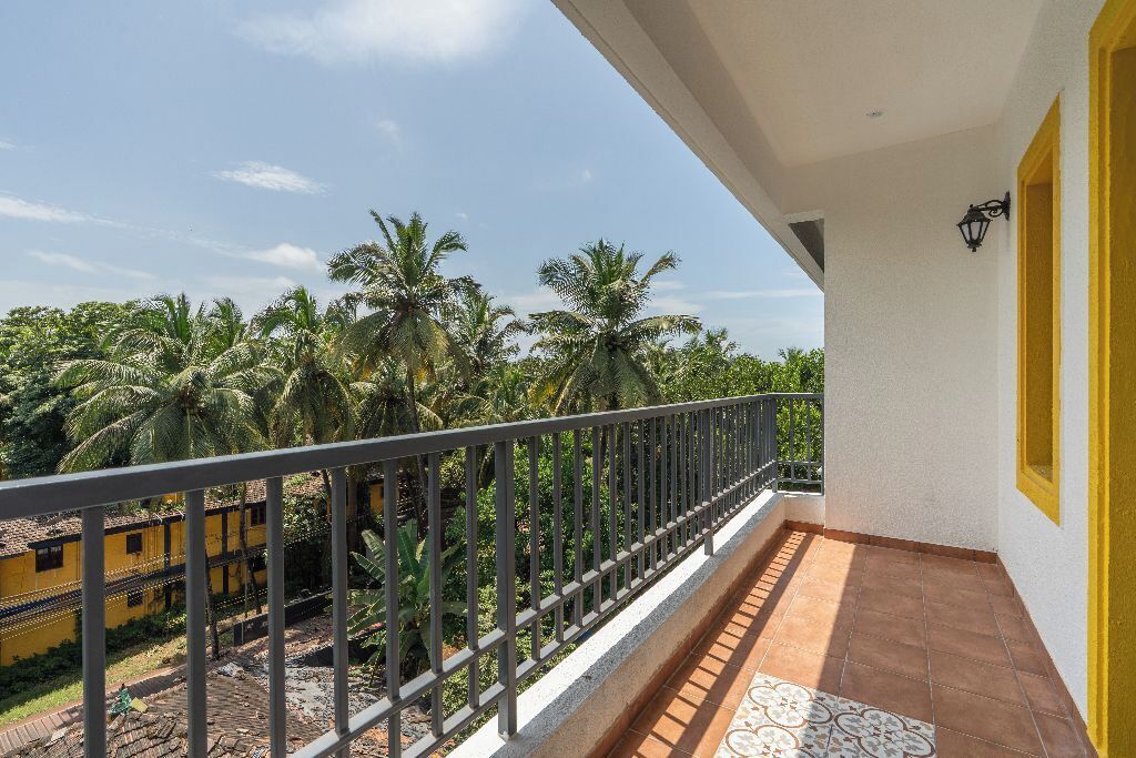 A balcony with a view of palm trees and a yellow building.
