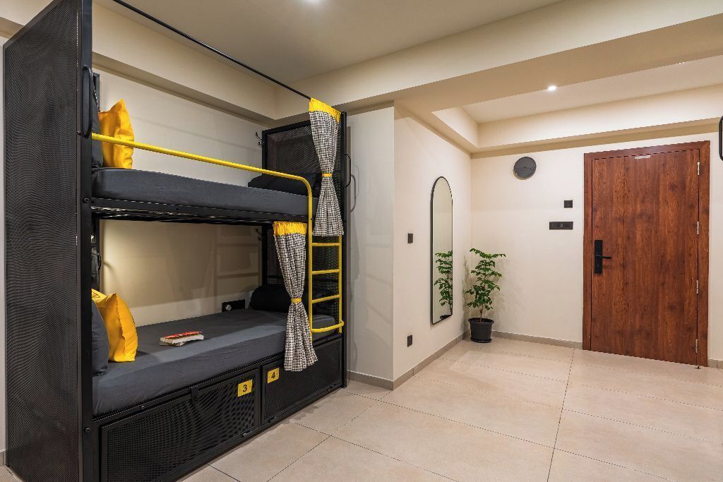 Un lit superposé avec des oreillers jaunes et une échelle, une plante en pot, une porte en bois et un miroir sur le mur.