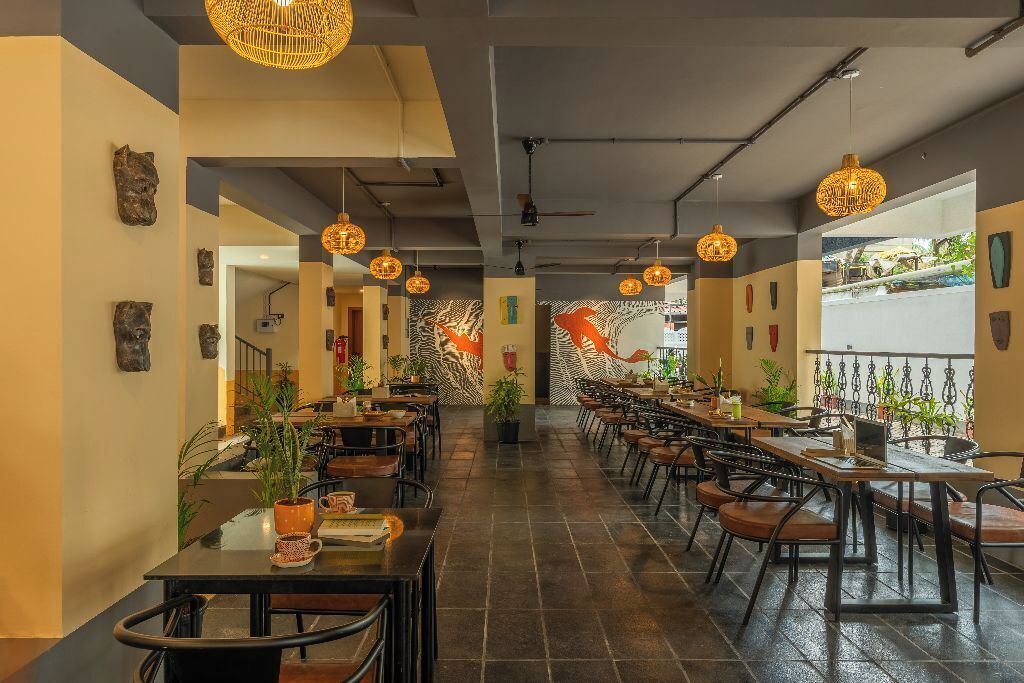 A spacious indoor dining area with multiple tables and chairs, decorative wall art, and hanging pendant lights.