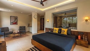 A modern bedroom with a large bed, a ceiling fan, a sitting area with two chairs, a coffee table, and a large window with a view. - The Hosteller Bam Goa Calangute (Calangute)