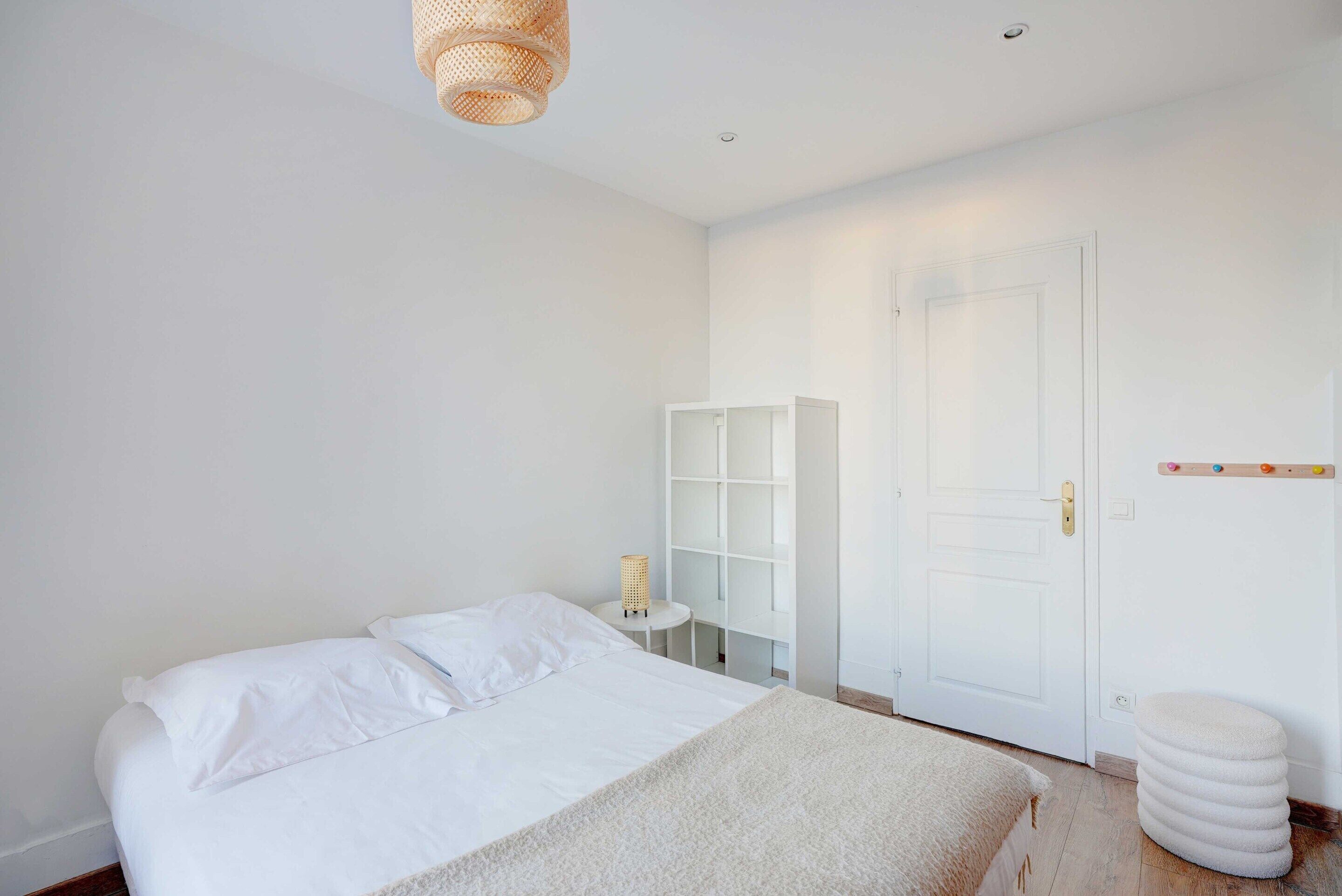A bedroom with a bed, a bedside table, a lamp, a wardrobe, and a door.