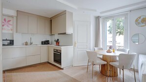 Een moderne keuken met witte kastjes, een ingebouwde oven, en een eethoek met een ronde houten tafel en witte stoelen.