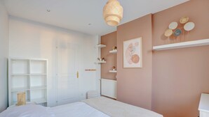 Een slaapkamer met een bed, een witte inbouwkast, een witte radiator en een wandplank met decoratieve objecten.