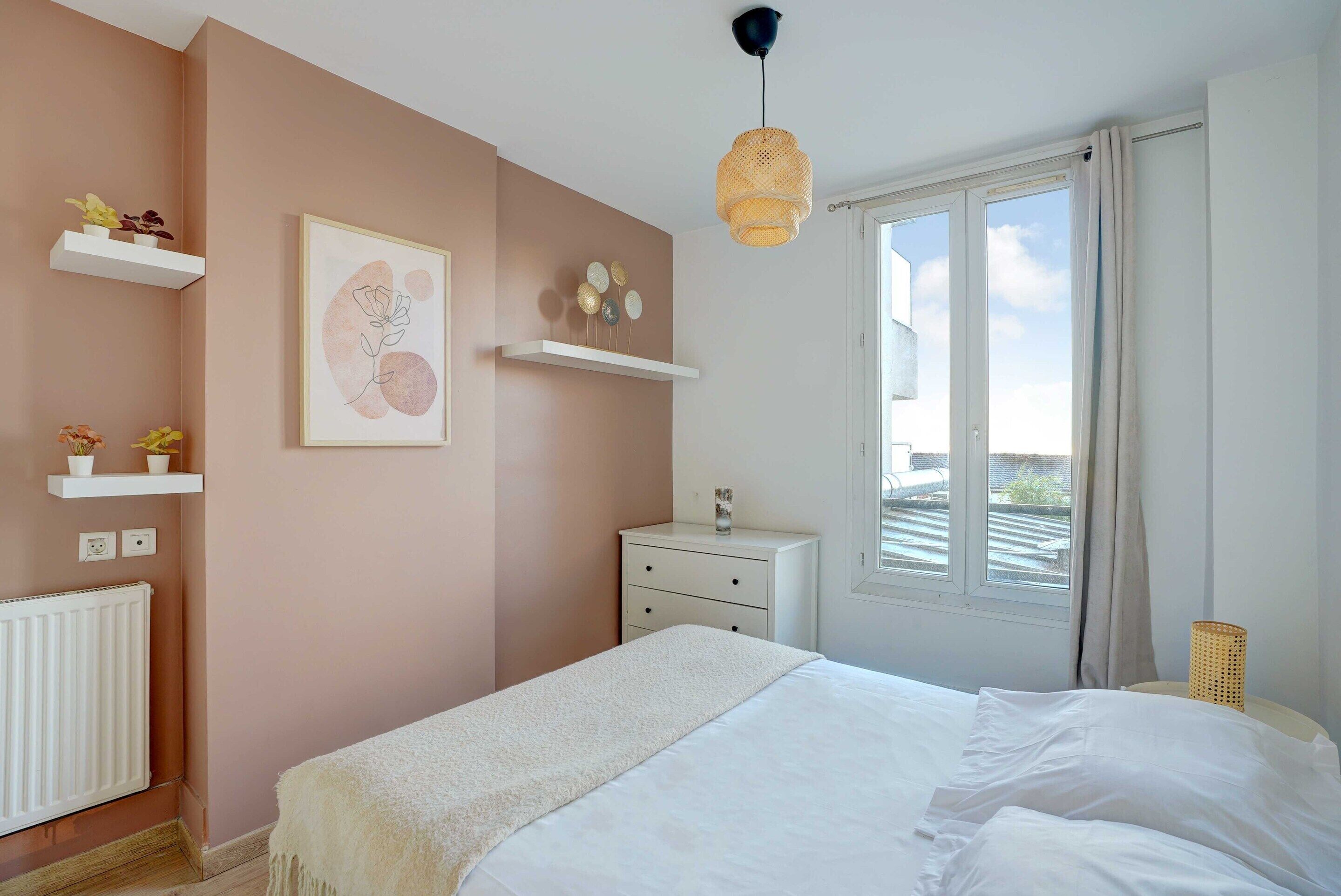 A bedroom with a bed, white dresser, wall art, and a window with curtains.