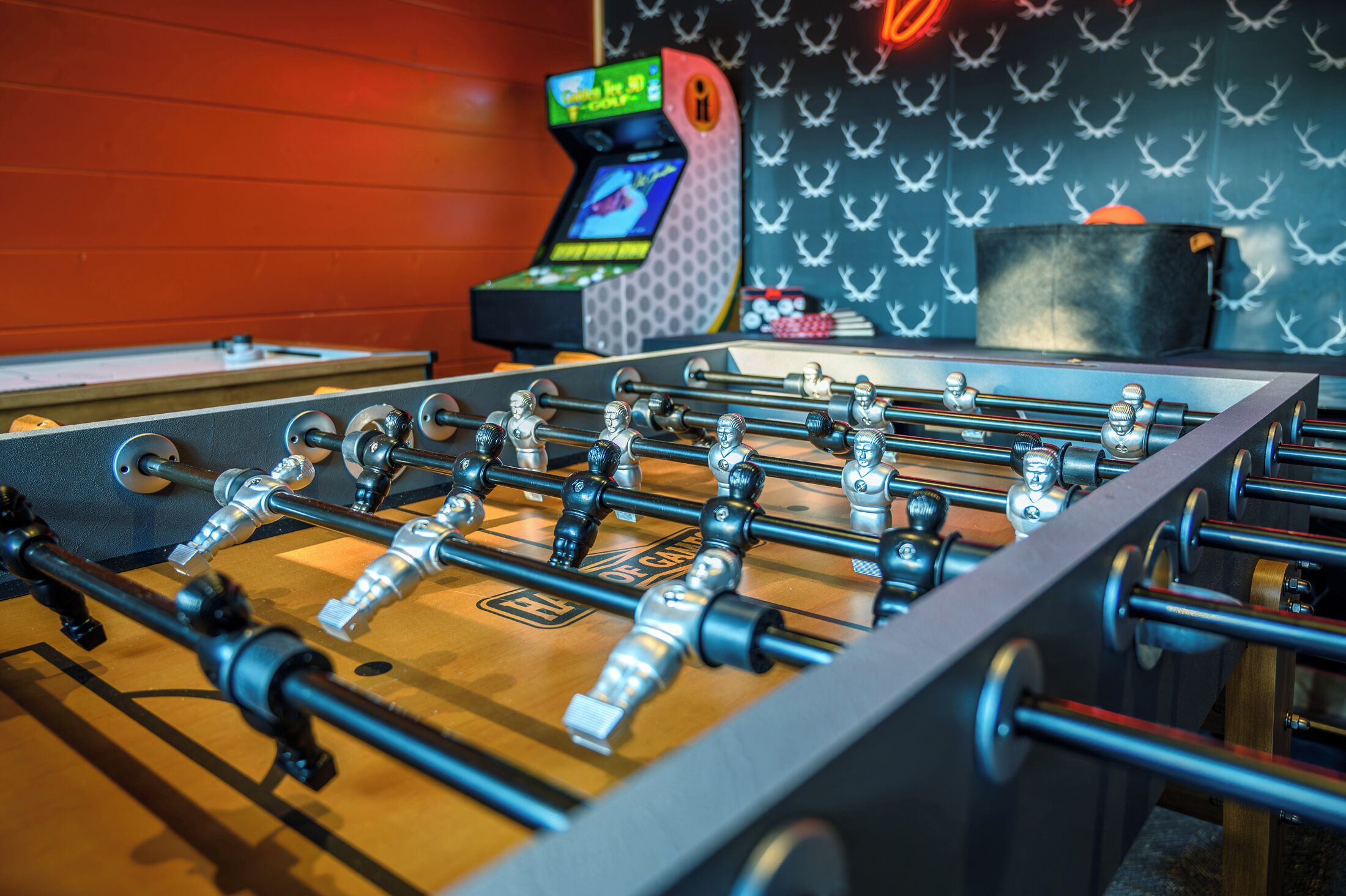 Een tafelvoetbaltafel met een houten basis en metalen stangen, voor een muur met een patroon en een neonbord.