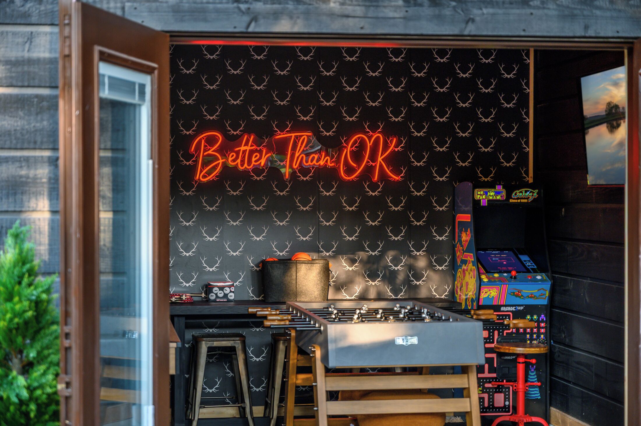 A room with a neon sign reading "Better Than OK," a foosball table, and arcade machines.