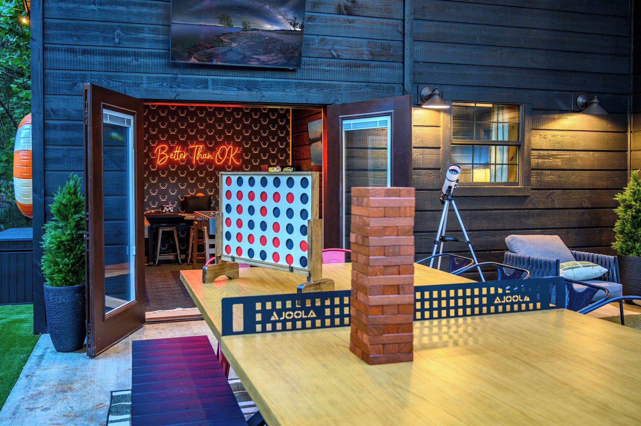 An outdoor seating area with a neon sign, a dartboard, and a telescope.