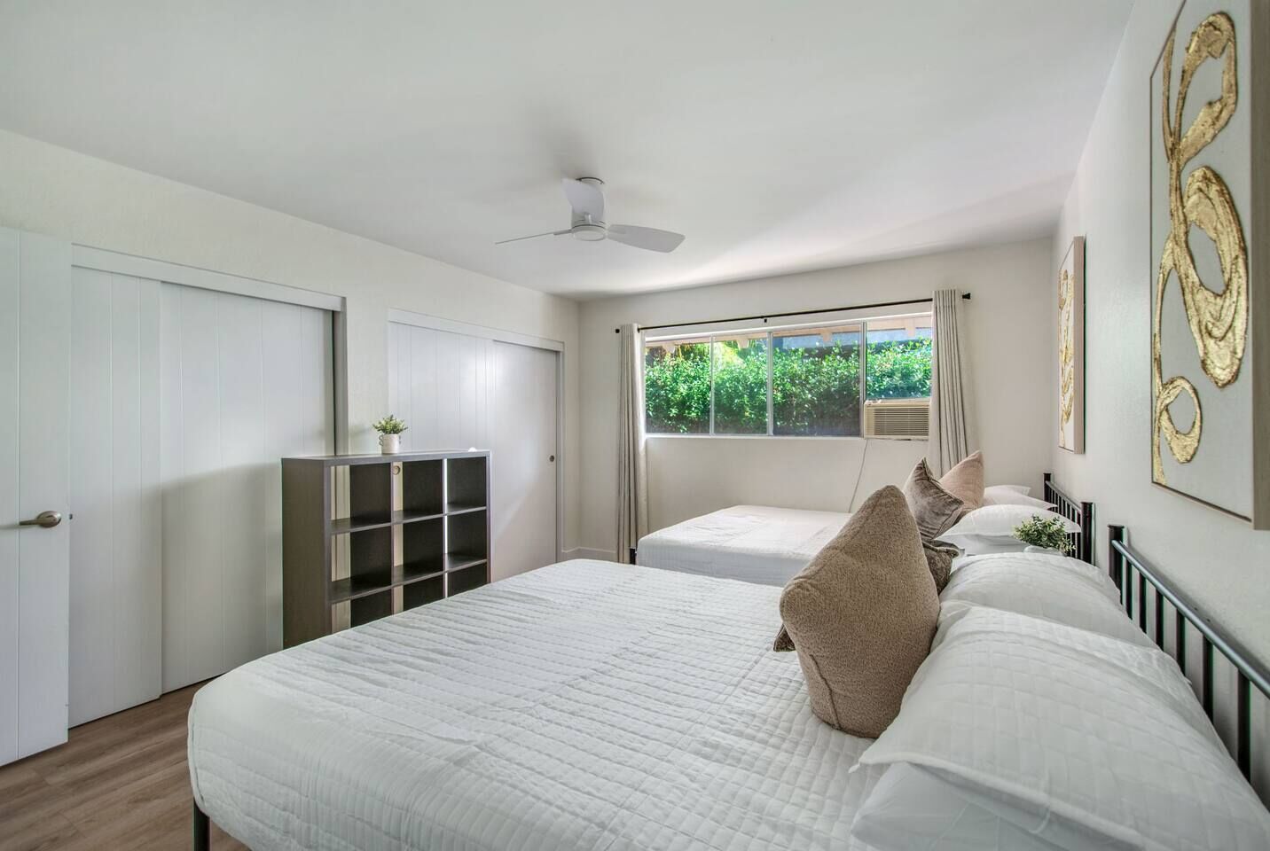 Un dormitorio con dos camas, un ventilador de techo, una ventana con cortinas y una planta en un estante.