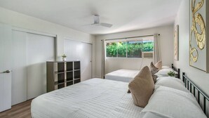 Ein Schlafzimmer mit zwei Betten, einem Deckenventilator, einem Fenster mit Vorhängen und einer Pflanze auf einem Regal.