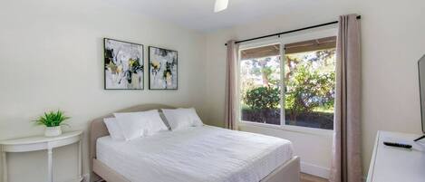 A bedroom with a bed, a nightstand, a plant, and a window with curtains.
