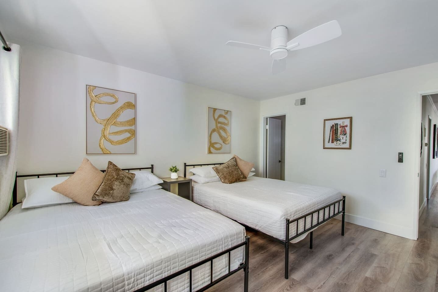 A hotel room with two beds, a ceiling fan, and artwork on the walls.