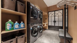 A laundry room with two front-loading washing machines, wicker baskets, and shelves with detergent bottles. - Kai Li Hotel (Wuhan)