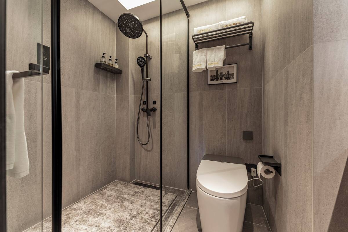 A modern bathroom with a glass-enclosed shower, a toilet, and a towel rack with towels.