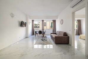 A modern living room with a sofa, a coffee table, a TV mounted on the wall, and a dining area with chairs and a table. - Posta Suites Flat in Ventimiglia (Ventimiglia)