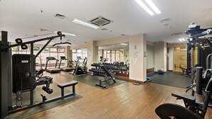 Een fitnessruimte met diverse trainingsapparaten, een loopband en een spiegelwand.