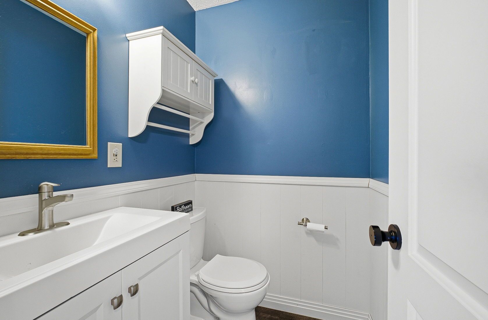 Un bagno con un lavandino bianco, un water e un armadietto bianco sopra il lavandino.