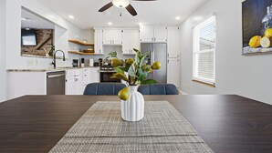 Une cuisine moderne avec des meubles blancs, un coin repas doté d’une table en bois foncé et un ventilateur de plafond.