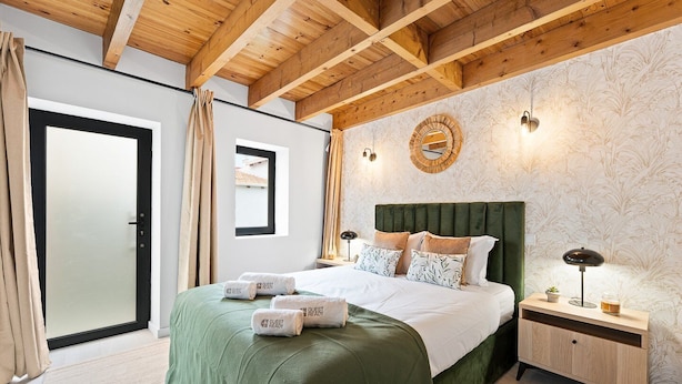 Une chambre d’hôtel avec un plafond en bois, un lit avec une literie verte, une table de chevet avec une lampe et un mur orné d’un miroir décoratif.