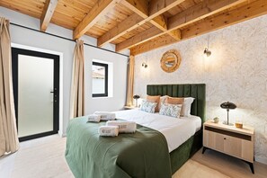 Habitación de hotel con techo de madera, cama con ropa de cama verde, mesita de noche con lámpara y espejo decorativo en la pared.