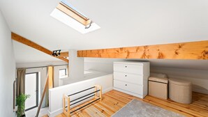 Une chambre de style loft moderne, dotée d’une lucarne, de poutres en bois, d’une commode blanche et d’un petit tapis.