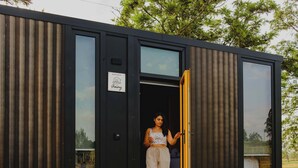 Una cabaña moderna y compacta con un amplio ventanal corredera, un pequeño espacio para sentarse al aire libre y un ventanal visible.