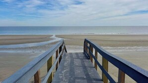 Een houten looppad dat naar een strand leidt, onder een heldere lucht.