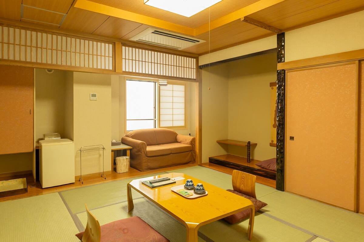 A traditional Japanese room with tatami flooring, a low table with cushions, a sofa, a cabinet, and a sliding door.