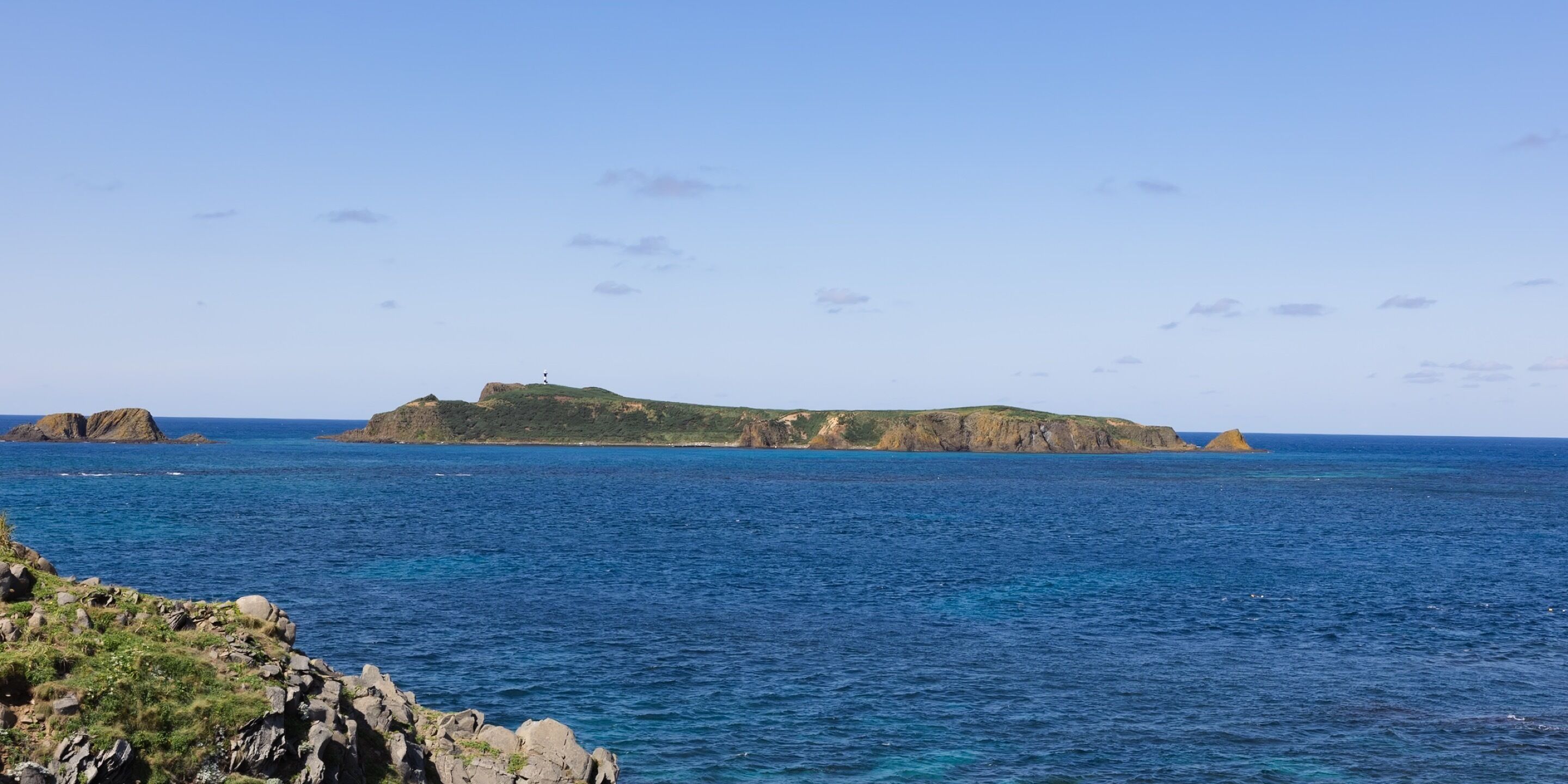 A coastal landscape with rocky terrain and a prominent hill with a lighthouse.