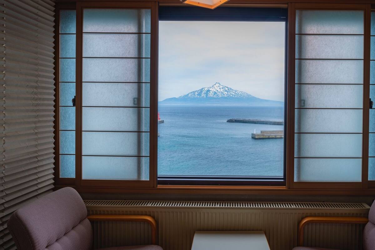 A room with a large window featuring shoji screens, a view of a mountain, and a dock.