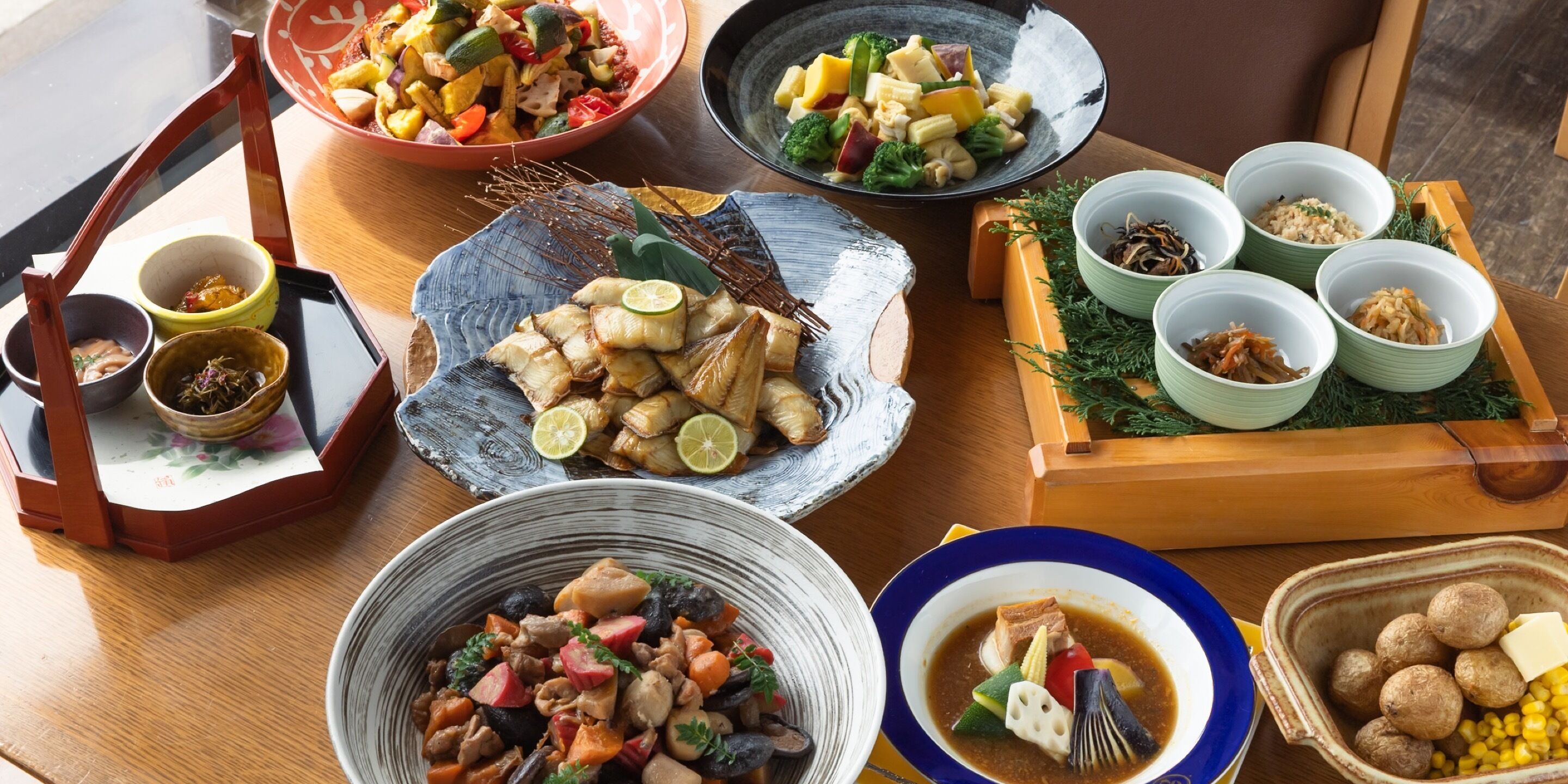 A variety of dishes on a wooden table, including a bowl of mixed vegetables, a plate of fish, and several small bowls containing different foods.