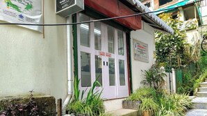A building with a white door and a sign above it. There are plants and a staircase leading up to the entrance. - Arthur's Inn (Gangtok)