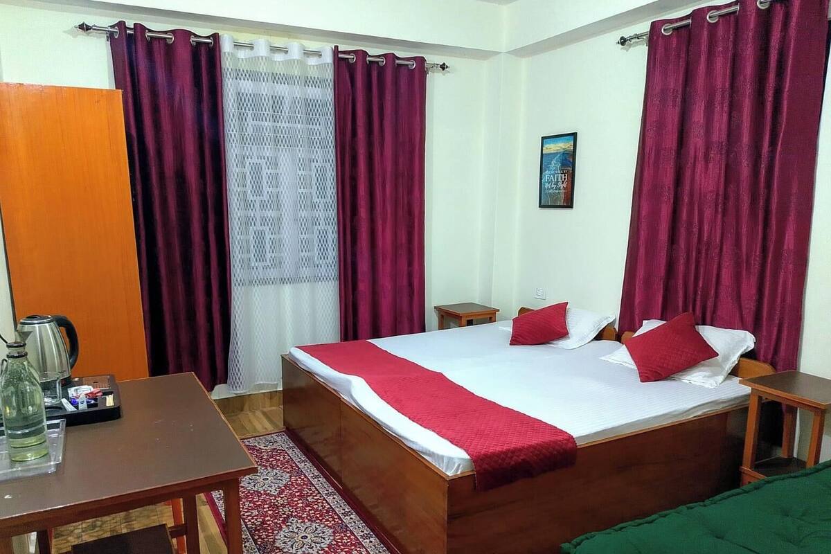 A bedroom with a wooden bed, red and white bedding, a small table with a kettle, and a red and white patterned rug.