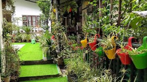 A narrow courtyard with artificial green turf, potted plants, and hanging planters. - Arthur's Inn (Gangtok)