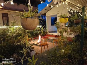 An outdoor patio area with hanging baskets, a fire pit, and potted plants.