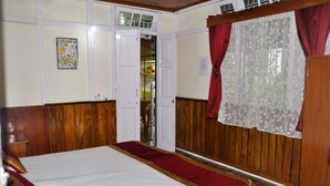 A room with wooden paneling, a bed with a red and white bedspread, a red and white chair, and a window with red curtains. - Arthur's Inn (Gangtok)