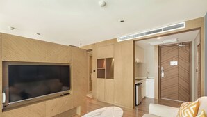 A modern living room with a large flat-screen TV, a marble coffee table, and a sofa with patterned cushions. - Studio in LaVita Condo in Rawai 7501 (Rawai)