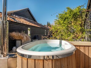 Ein Whirlpool auf einer Holzterrasse, im Hintergrund ein Haus.