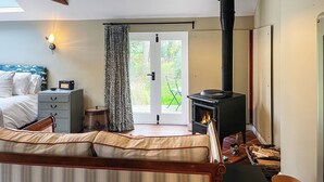 A bedroom with a bed, a sofa, a fireplace, a window, and a door leading outside. - The Butterchurn - UK50805 (Cratfield, near Laxfield)