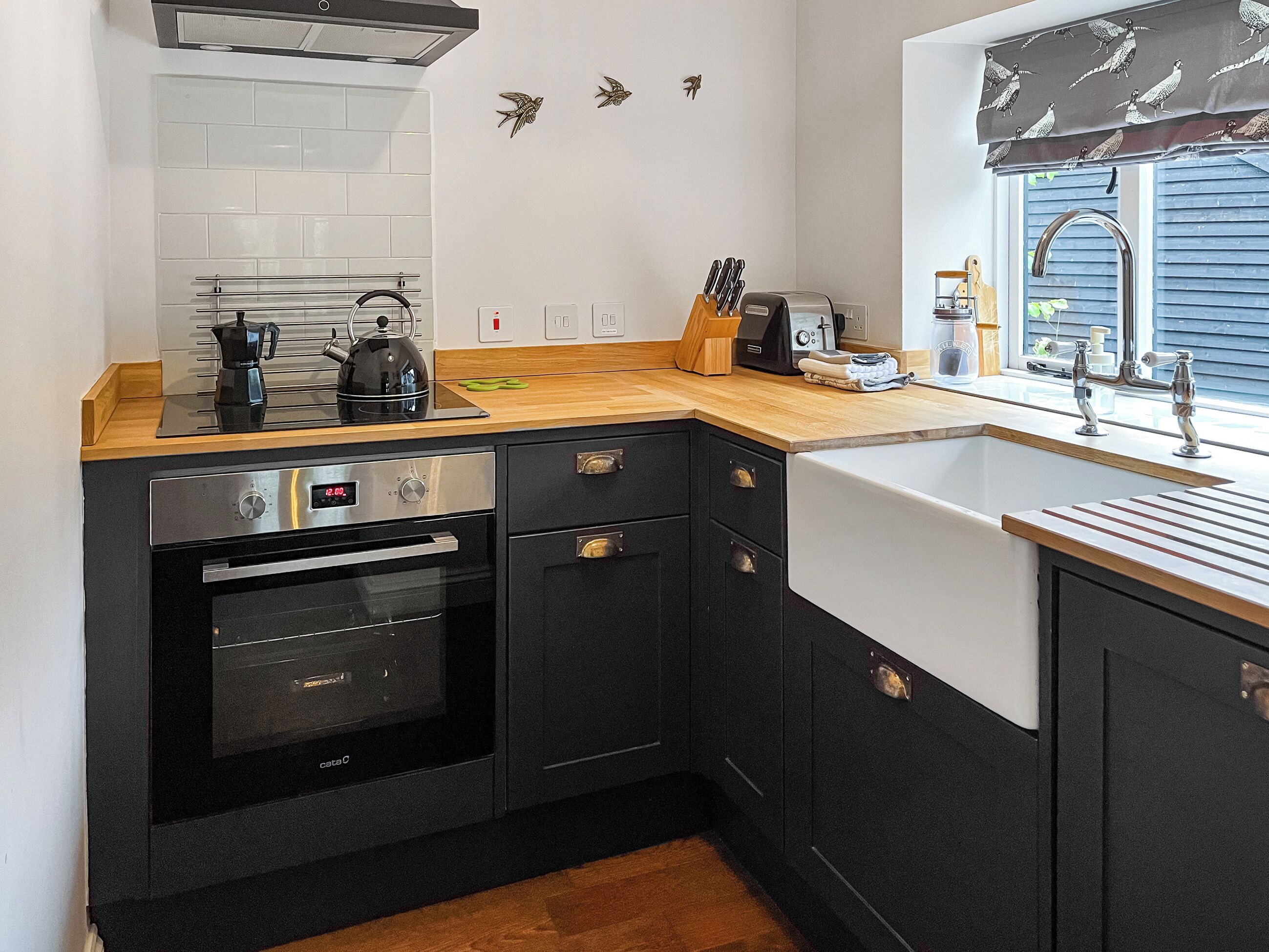 A compact kitchen with a stove, oven, sink, and wooden countertop.