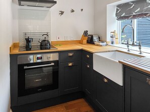 Eine kleine Küche mit Herd, Backofen, Spüle und Arbeitsplatte aus Holz.