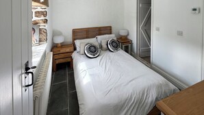 Une chambre à coucher avec un lit, des tables de chevet, une commode, un radiateur, une armoire et un mur en pierre.