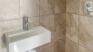 Une salle de bain avec un lavabo blanc, un robinet chromé et des toilettes suspendues.