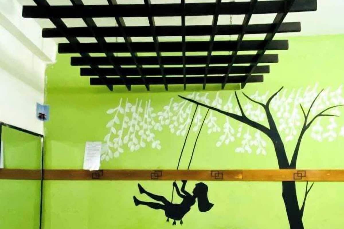 A room with a bed, a green wall with a tree mural, a wooden ceiling, and a small table with a red tablecloth.