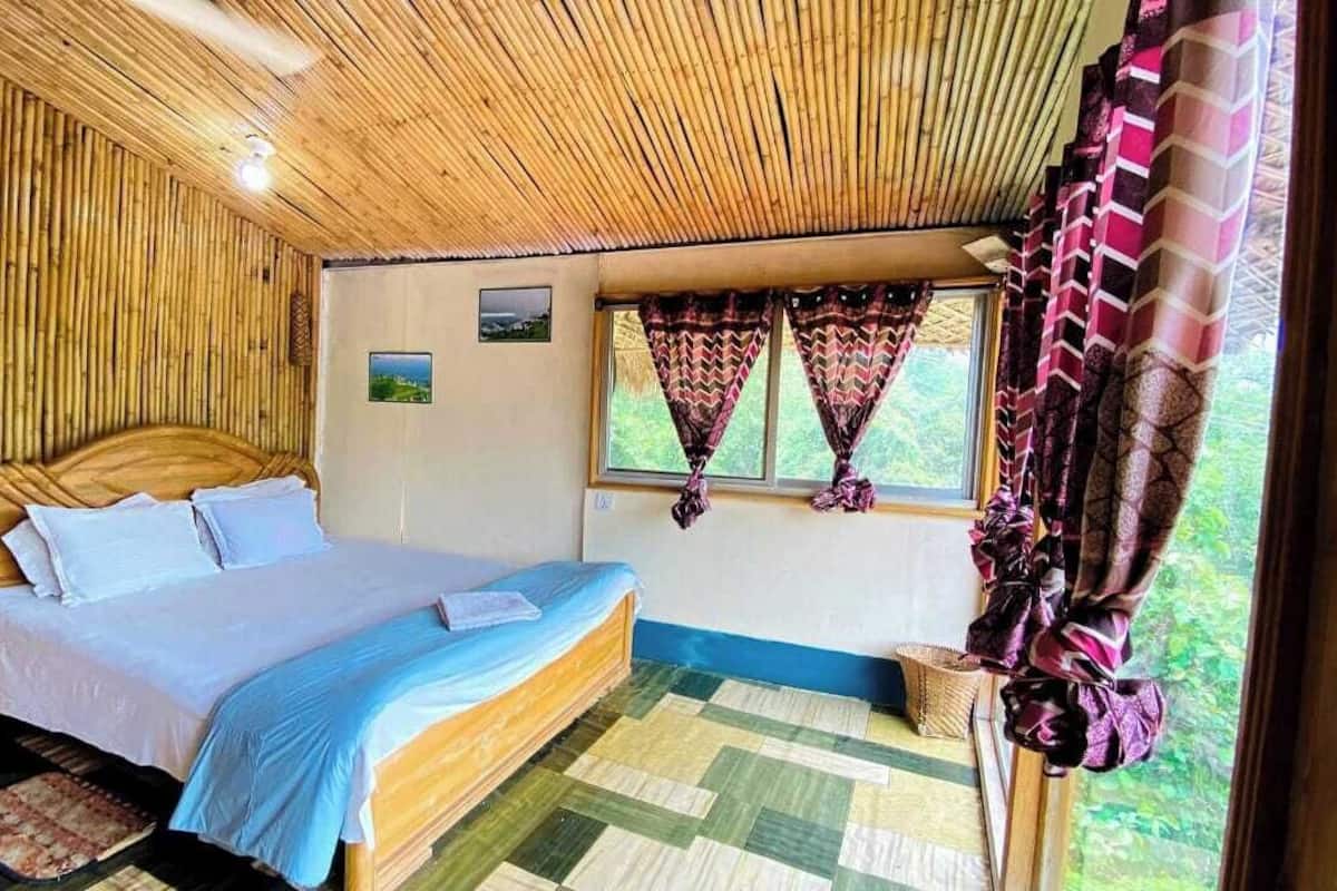A room with a bed, wooden walls, a window with curtains, and a view of greenery outside.