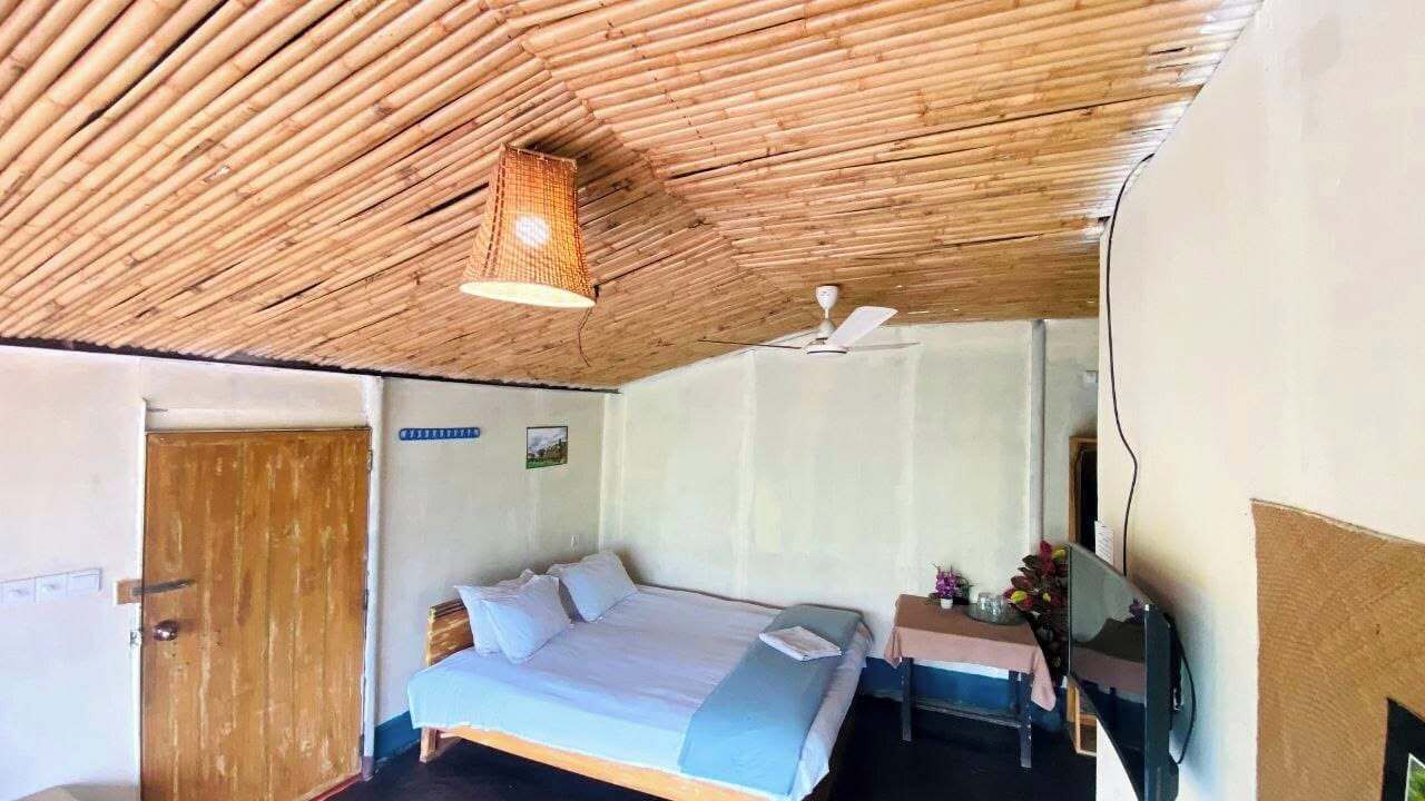 Una habitación con cama, mesita de noche, televisor montado en la pared y ventilador de techo.