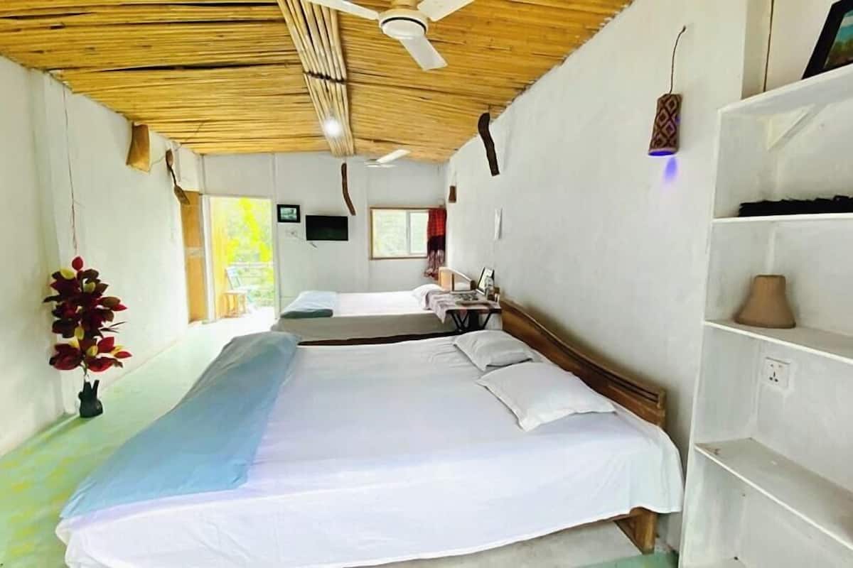 A room with two beds, a ceiling fan, a window, and a shelf with a lamp.
