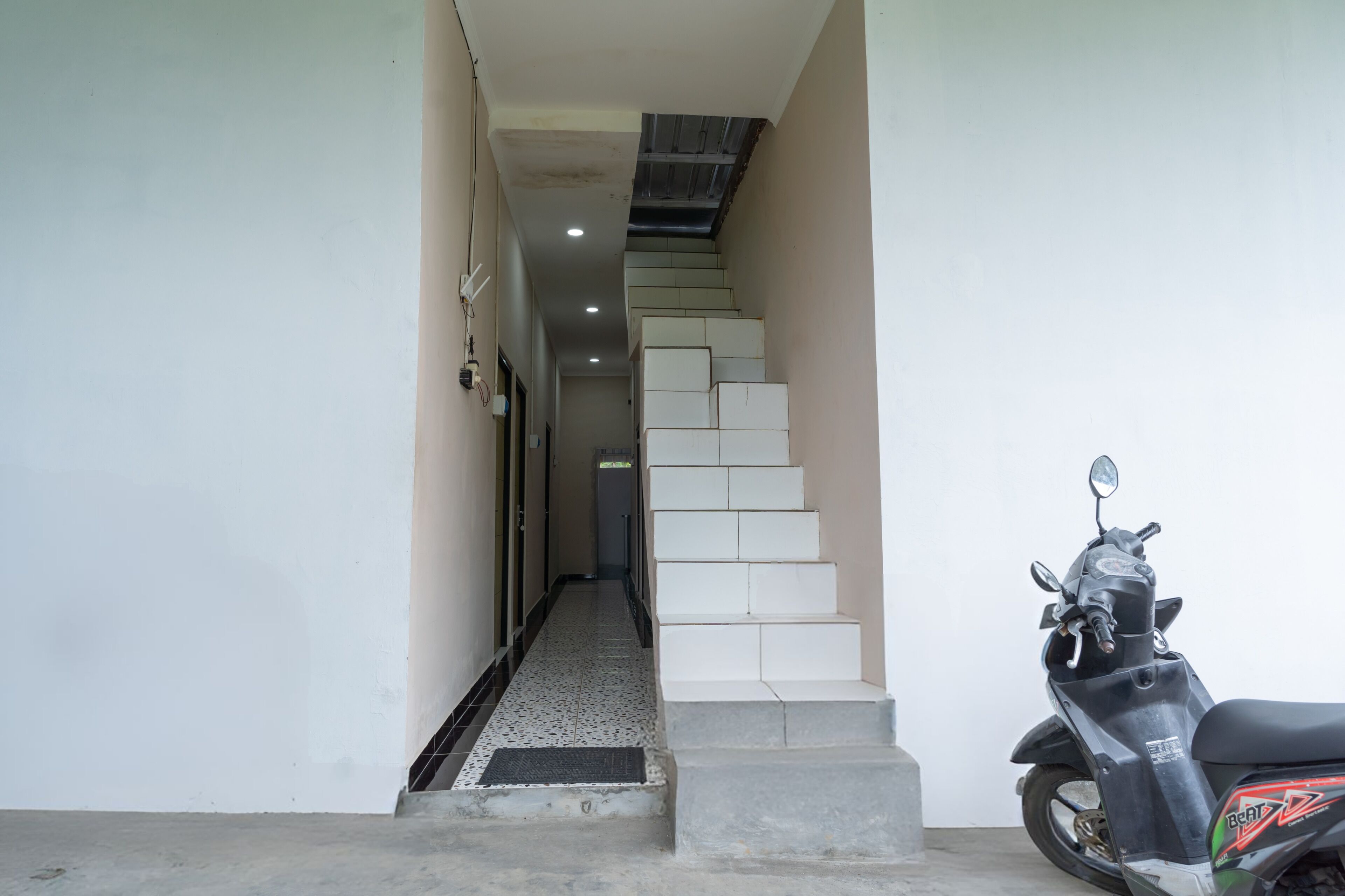 Um corredor estreito com piso ladrilhado que leva a uma escadaria. Uma scooter está estacionada na base da escada.