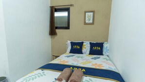 A neatly made bed with a floral bedspread, two pillows with 'ARBA' branding, and two rolled towels on the bed. - ELBA Guesthouse Near UNNES by ARBA (Semarang)