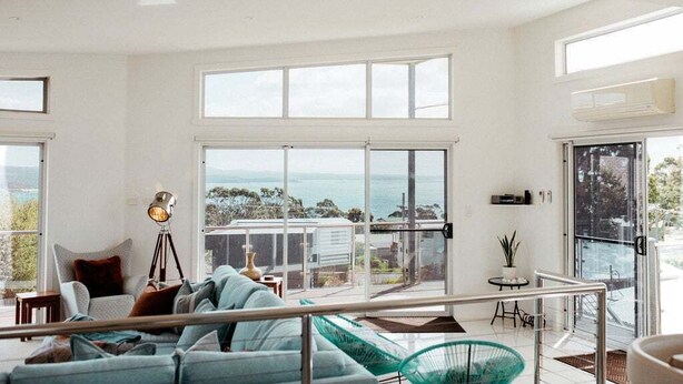 A spacious living area with a large sliding glass door leading to a balcony, a sofa, a floor lamp, and a view of the ocean.